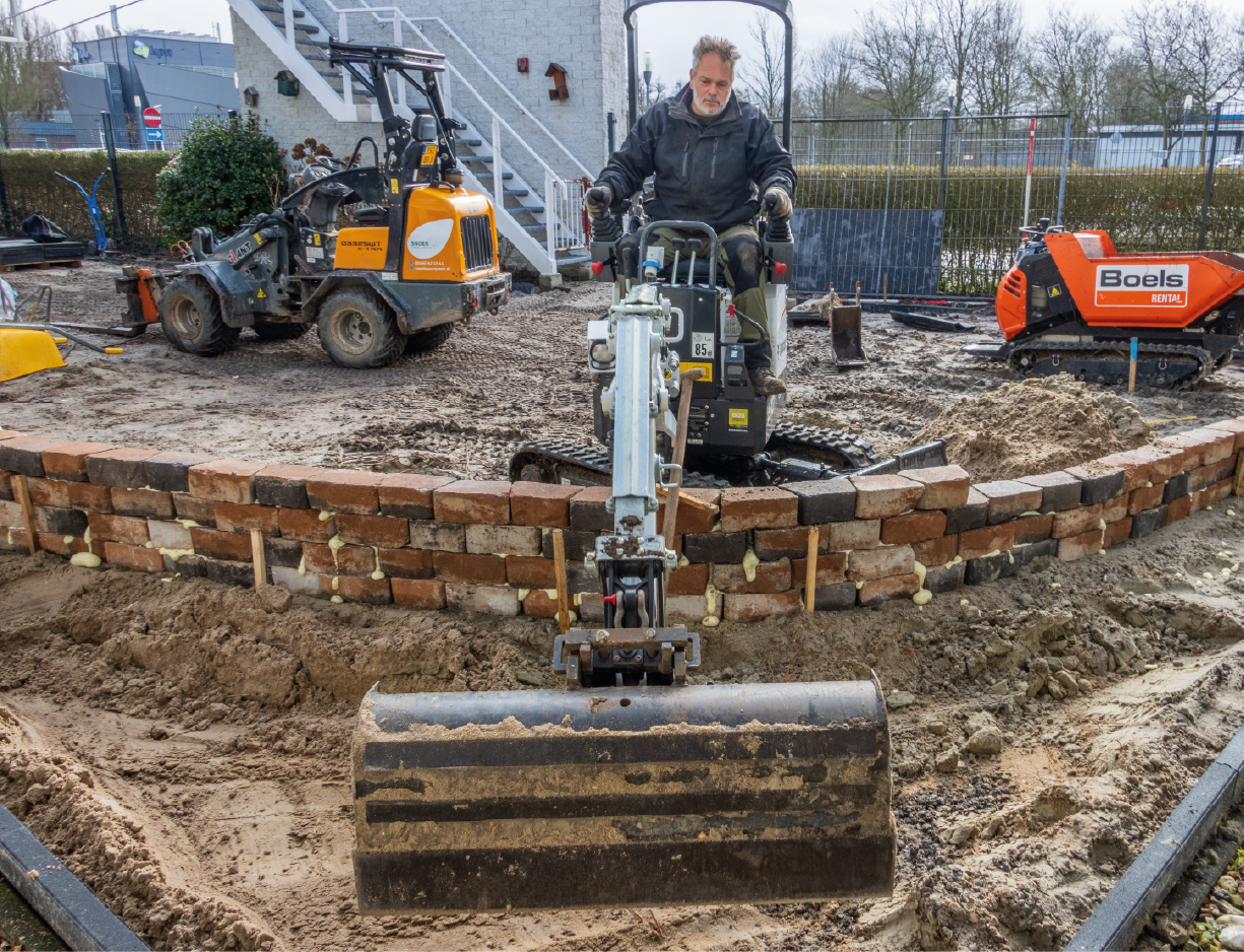 http://Man%20op%20graafmachine%20die%20achter%20een%20stenen%20muurtje%20graaft%20en%20een%20terrein%20aanlegt