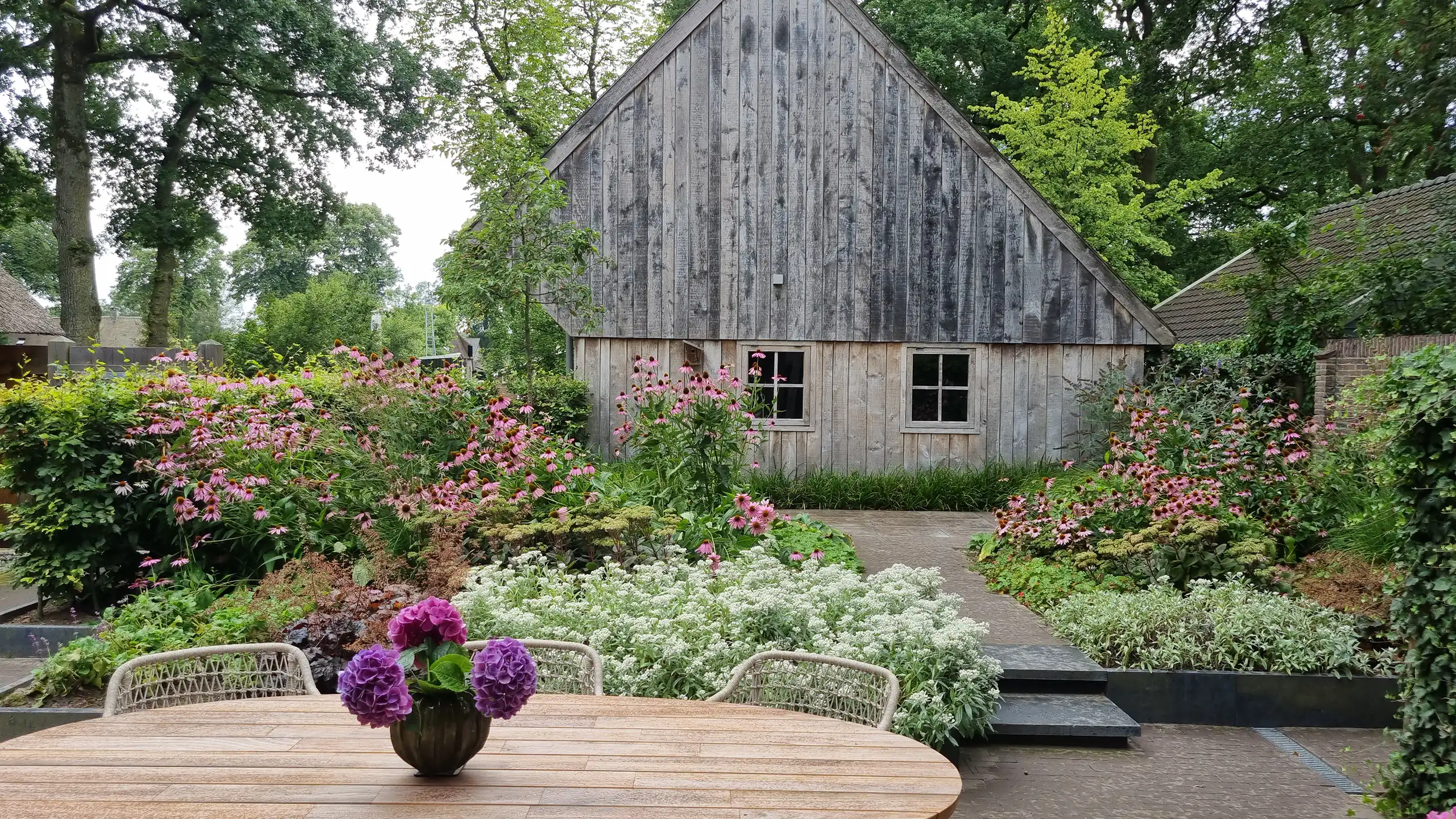 http://Tuintafel%20met%20hortensia%20bloemen%20op%20tafel%20met%20daarachter%20schuur%20en%20plantenborder