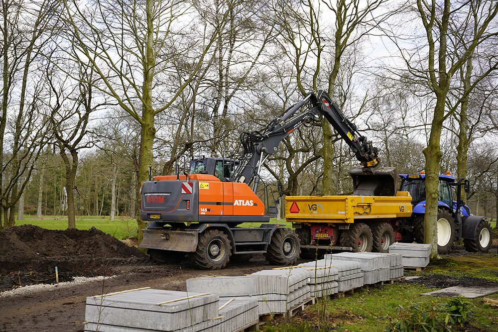 Kraan die grond uit een aanhanger van een trekker graaft in een groene omgeving